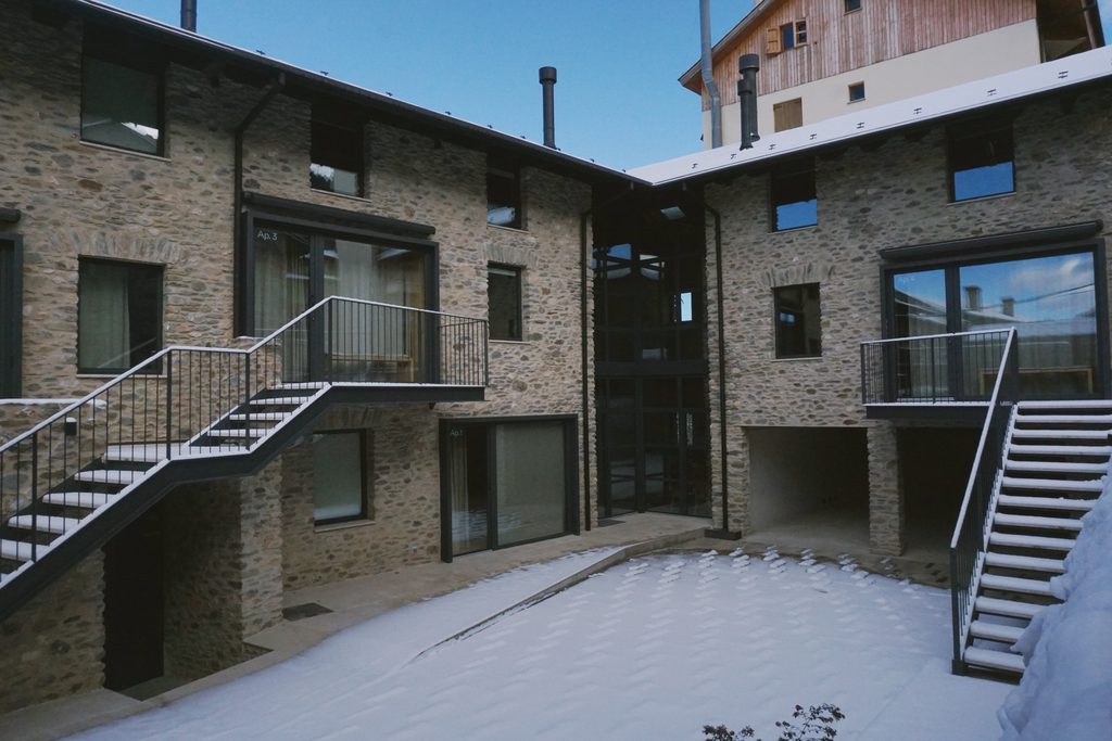 Patio nevado entre las fachadas de piedra con escaleras exteriores