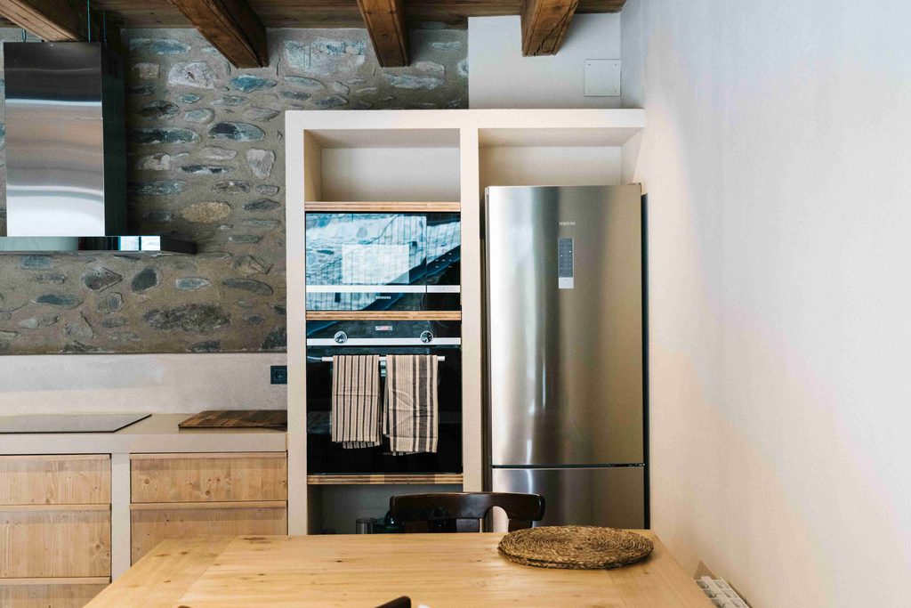 Cocina con frigorífico, horno y pared de piedra