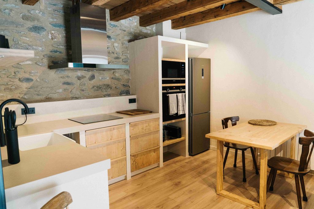 Cocina con mesa de madera para dos y pared de piedra