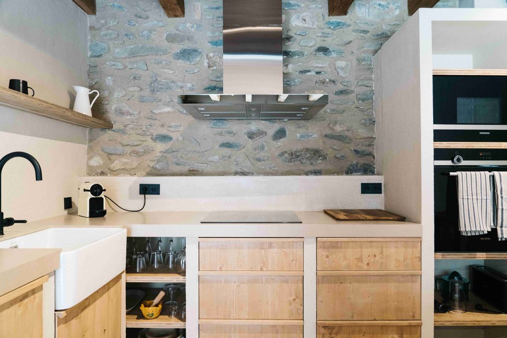 Cocina con fregadero de cerámica, placa y pared de piedra