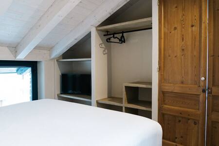 Dormitorio abuhardillado con cama doble, armario abierto y televisor