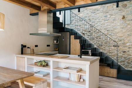 Cocina con isla blanca, campana y escalera junto a una pared de piedra