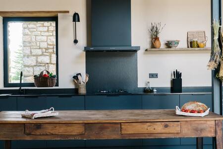 Cocina con encimera azul oscuro, estantes y mesa de madera