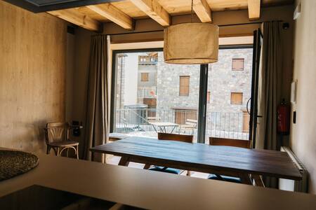 Comedor con mesa de madera, lámpara colgante y ventanal con vistas al pueblo