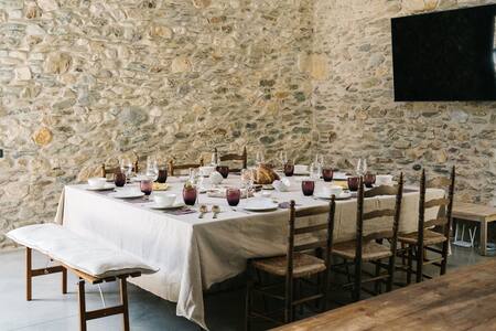 Comedor común con mesa larga puesta y pared de piedra