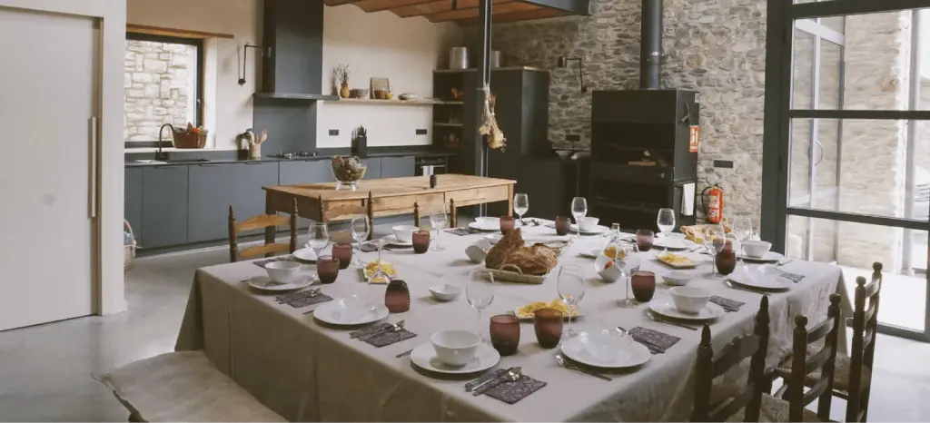 Comedor de Mas Cal Rus con mesa larga preparada, cocina abierta y paredes de piedra